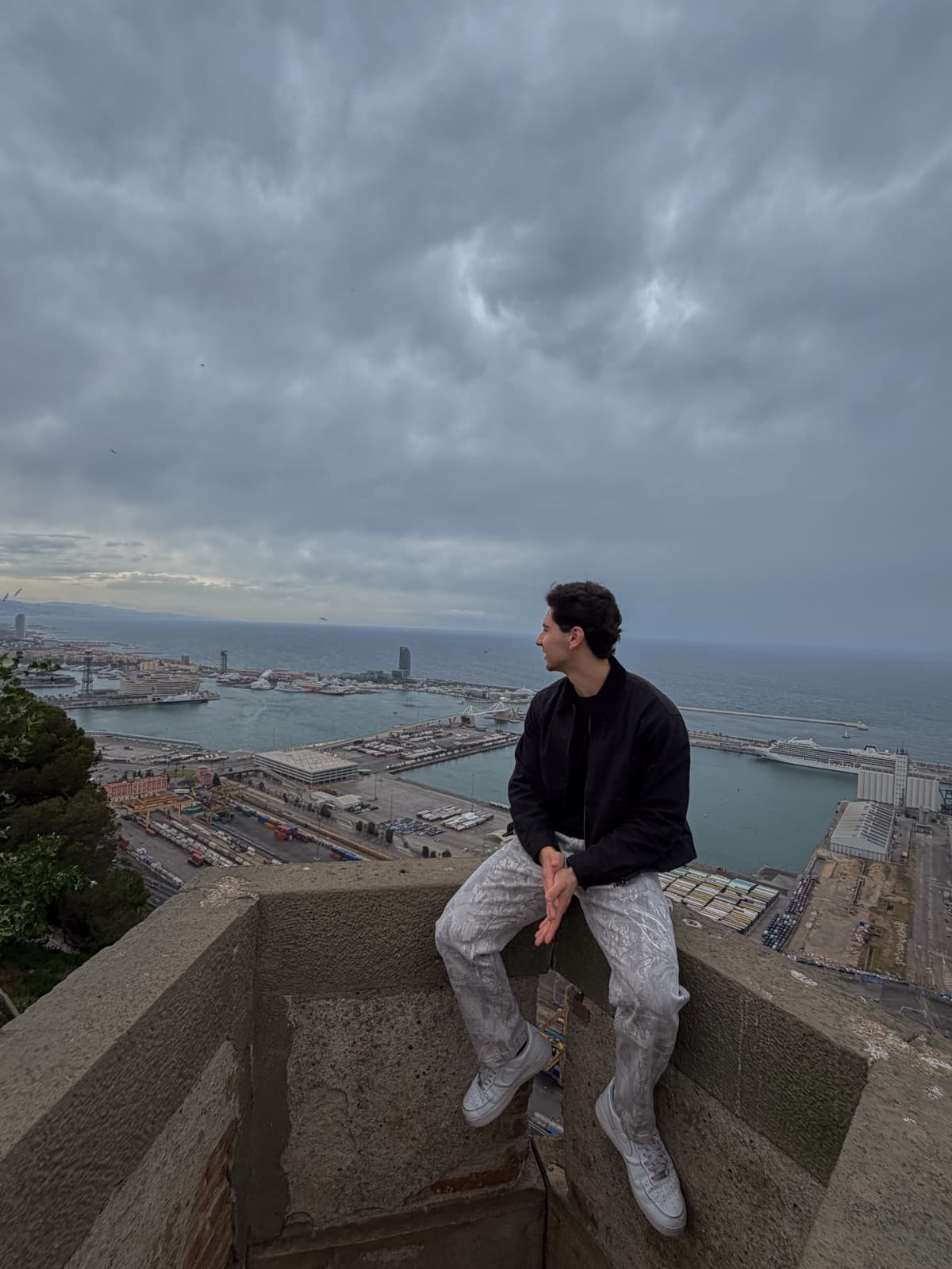 Sitting on a lookout wall above the port of Barcelona under a storm sky